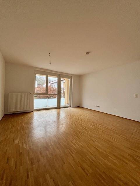 Großes, helles Zimmer mit Parkettboden und Zugang zu einem sonnigen Außenbereich.