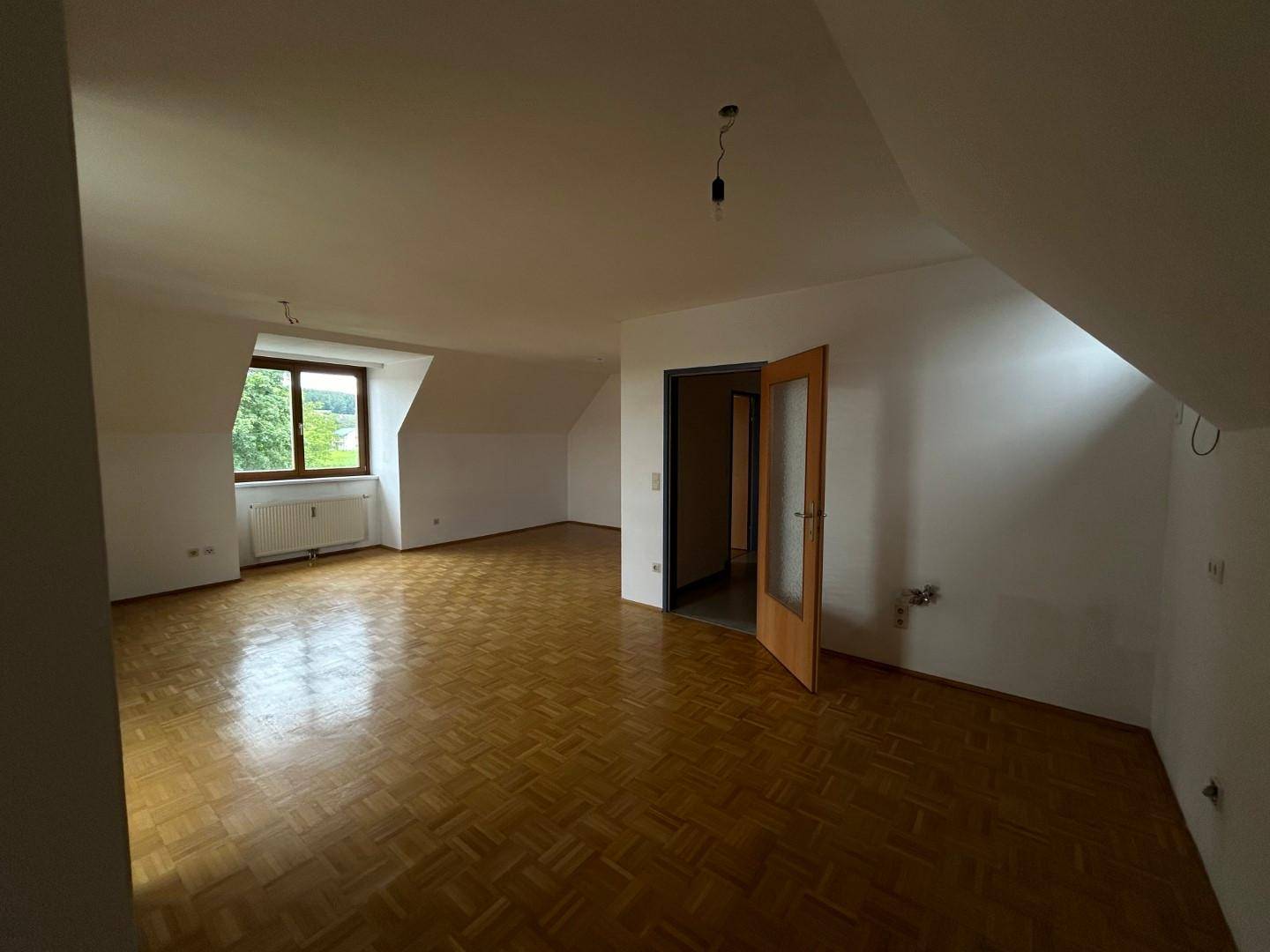 Geräumiger Wohnbereich mit Parkettboden, Dachschrägen und Blick ins Grüne.