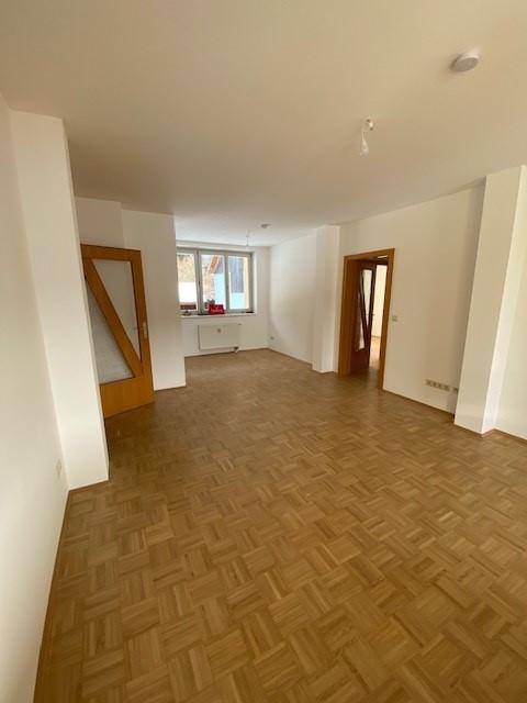 Geräumiges Wohnzimmer mit klassischem Parkettboden und viel Tageslicht durch die Fenster.