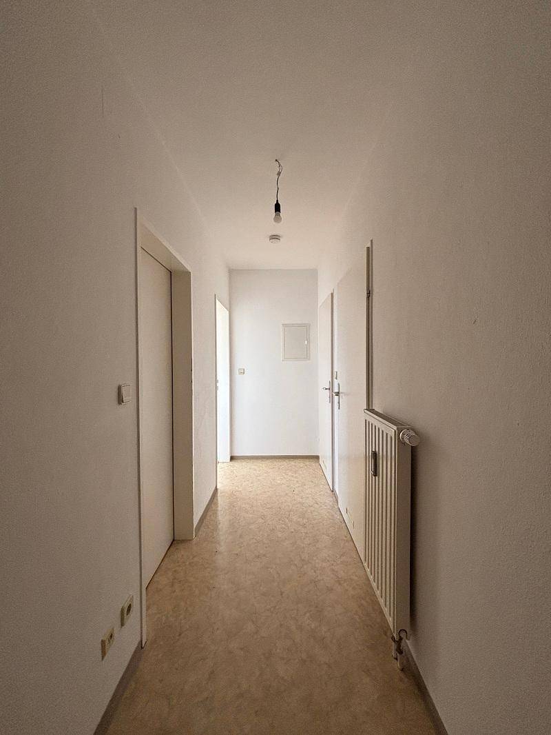 Langer, schmaler Flur mit hellen Wänden, funktionalem Heizkörper und mehreren Türen zu angrenzenden Räumen.