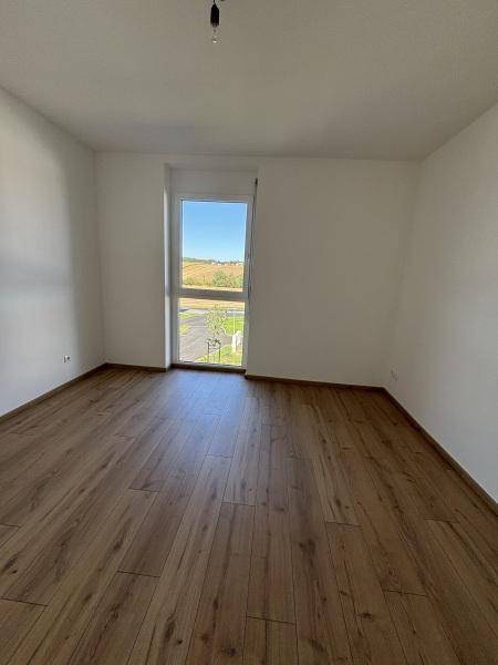 Helles Zimmer mit Holzplankenboden und großem Fenster, das viel Tageslicht hereinlässt.