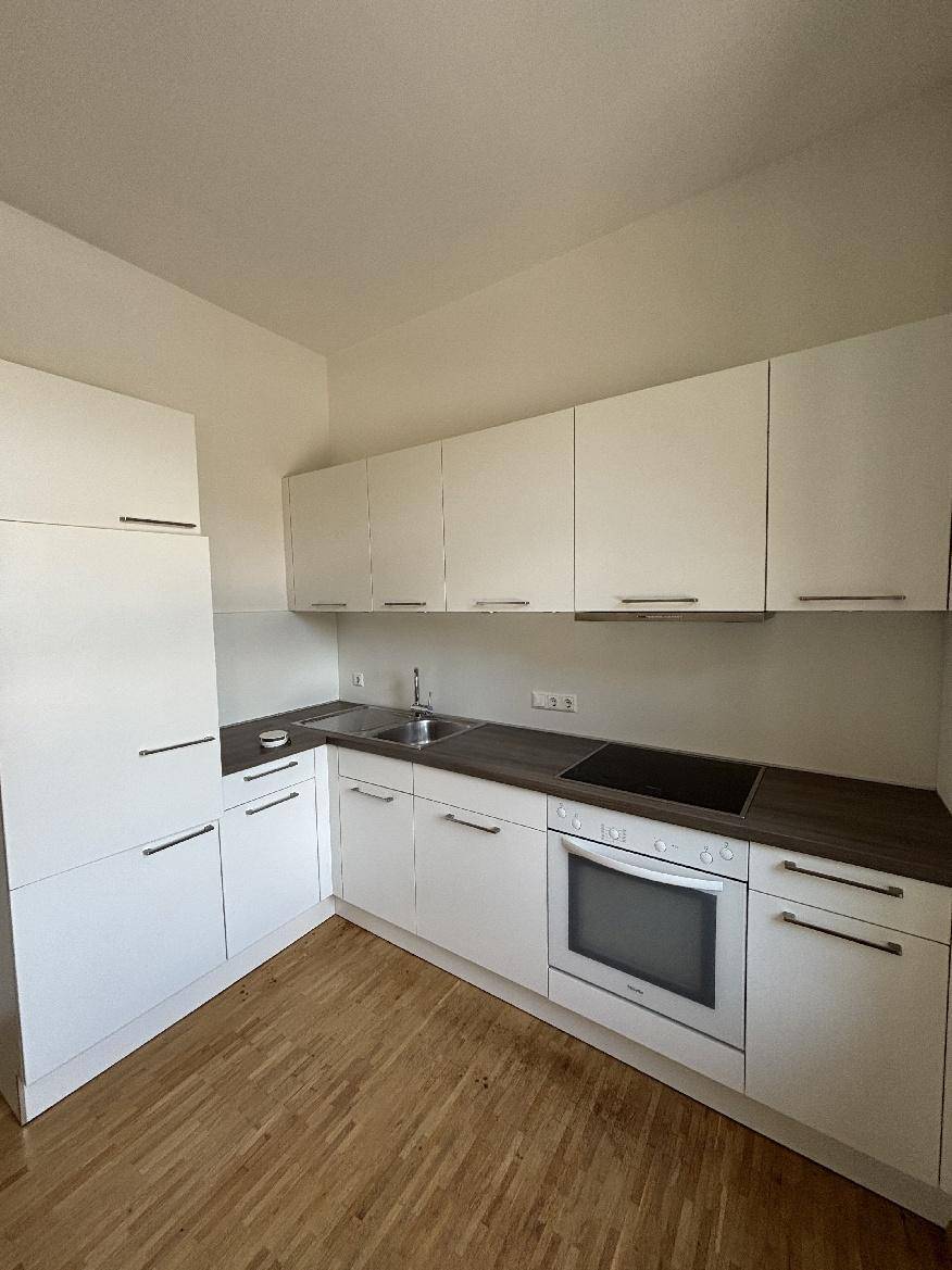 Moderne Einbauküche mit weißen Schränken, dunkler Arbeitsplatte und integriertem Backofen.