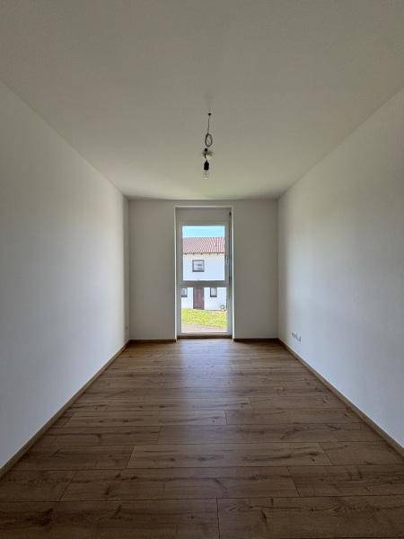 Leeres Zimmer mit Holzboden und einem großen Fenster, das viel natürliches Licht hereinlässt.