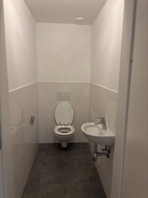 Modernes Gäste-WC mit Wand-WC, kleinem Waschbecken und hellen Fliesen an den Wänden.