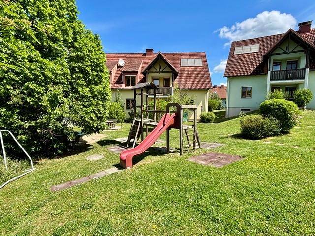 Großer Gartenbereich mit Kinderspielplatz und Rutsche, umgeben von Grünflächen und Bäumen.