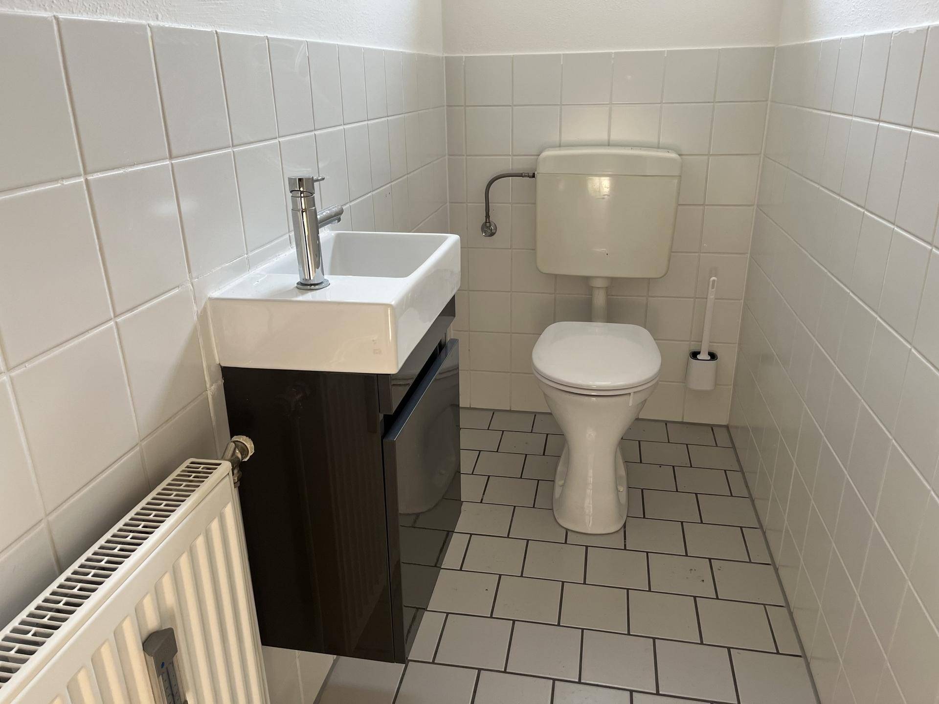 Modernisiertes Gäste-WC mit kleinem Waschbecken und Toilette, hell gefliest.