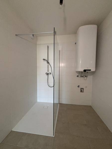Modernes Badezimmer mit ebenerdiger Dusche, Glasabtrennung und einem Warmwasserboiler.