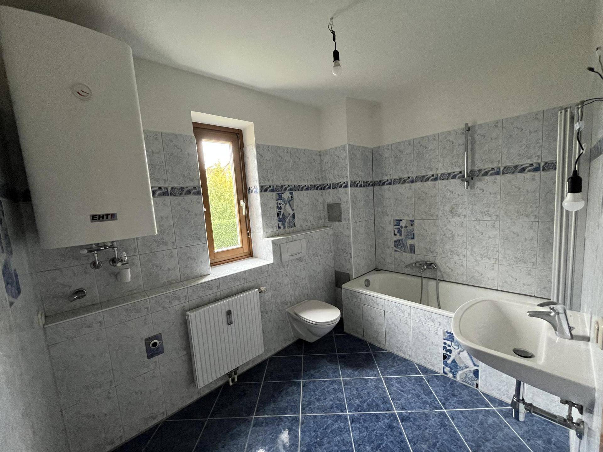 Badezimmer mit blauen und weißen Fliesen, Badewanne, WC und Fenster für Tageslicht.