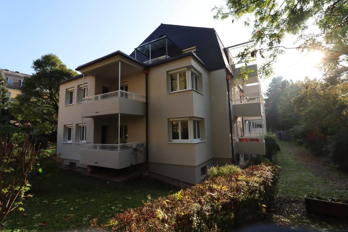Seitenansicht eines Wohnhauses mit mehreren Balkonen und umgebender grüner Landschaft.