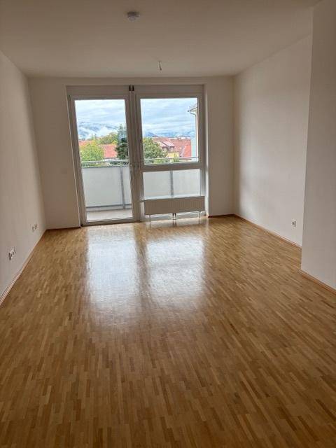 Helles Zimmer mit Parkettboden und Zugang zu einem Balkon, ausgestattet mit einem Heizkörper.