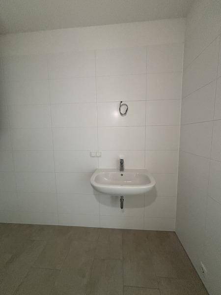 Helles Badezimmer mit einem einzelnen Waschbecken und weißen Fliesen, bereit für die Endausstattung.