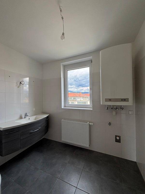 Helles Badezimmer mit Fenster, modernem Waschtisch und Wandheizkörper, dunkler Fliesenboden.