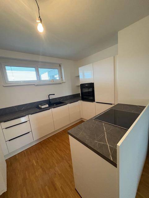 Moderne Küche mit weißen Schränken, dunklen Arbeitsplatten und Holzboden, ausgestattet mit einem Fenster und Kochinsel.