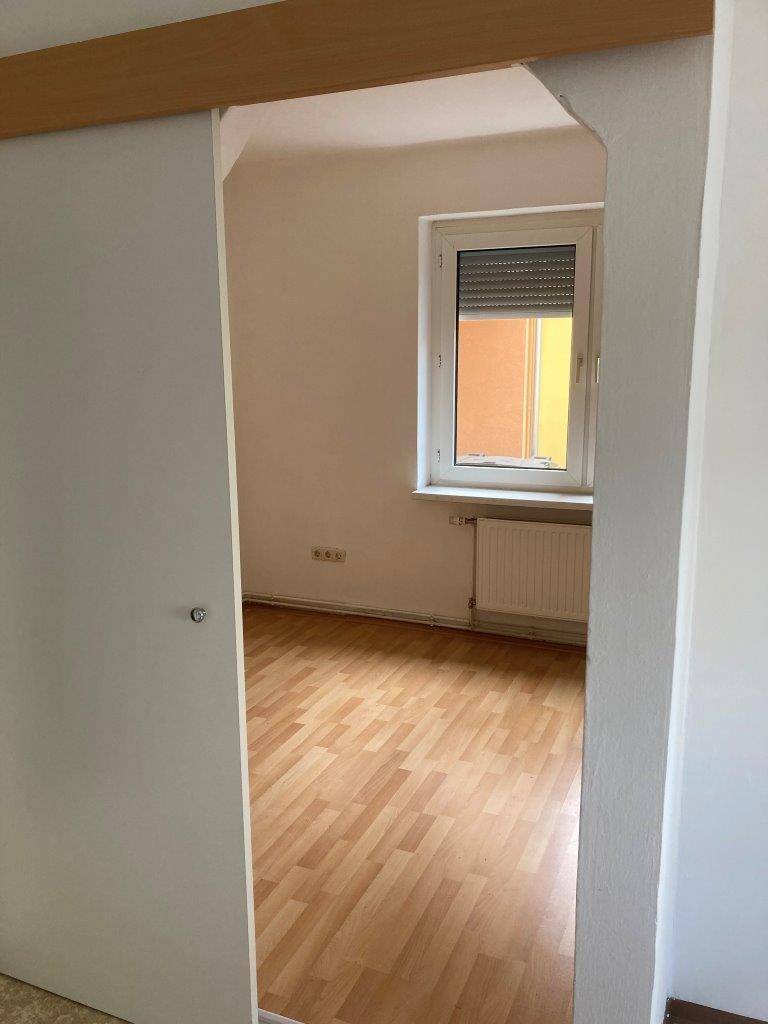 Helles Zimmer mit Laminatboden und Fenster mit Rollladen.