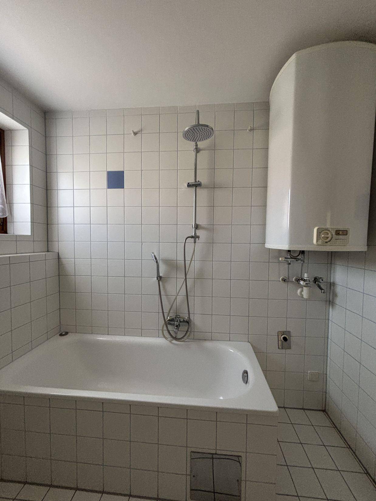Badezimmer mit Badewanne, Duschkopf und einem Warmwasserboiler an der Wand.