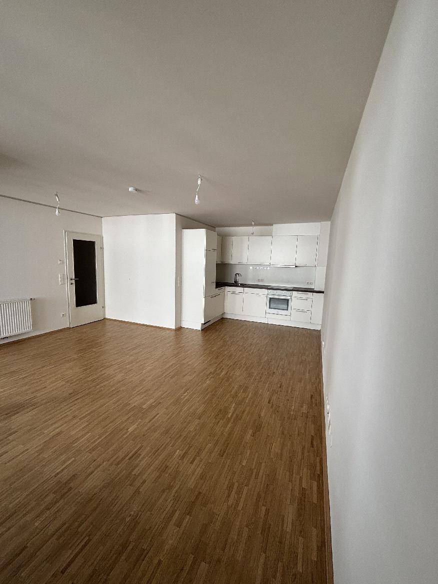 Offener Wohnbereich mit Holzparkettboden und integrierter, moderner weißer Küche.