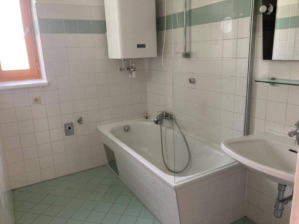 Badezimmer mit Badewanne, Waschbecken und Wandheizkörper in hellen Fliesenfarben.