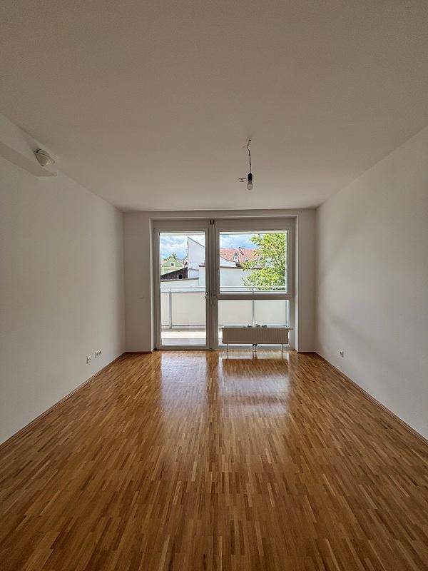 Heller Wohnraum mit Parkettboden und großen Fenstern, die Zugang zu einem kleinen Balkon bieten.