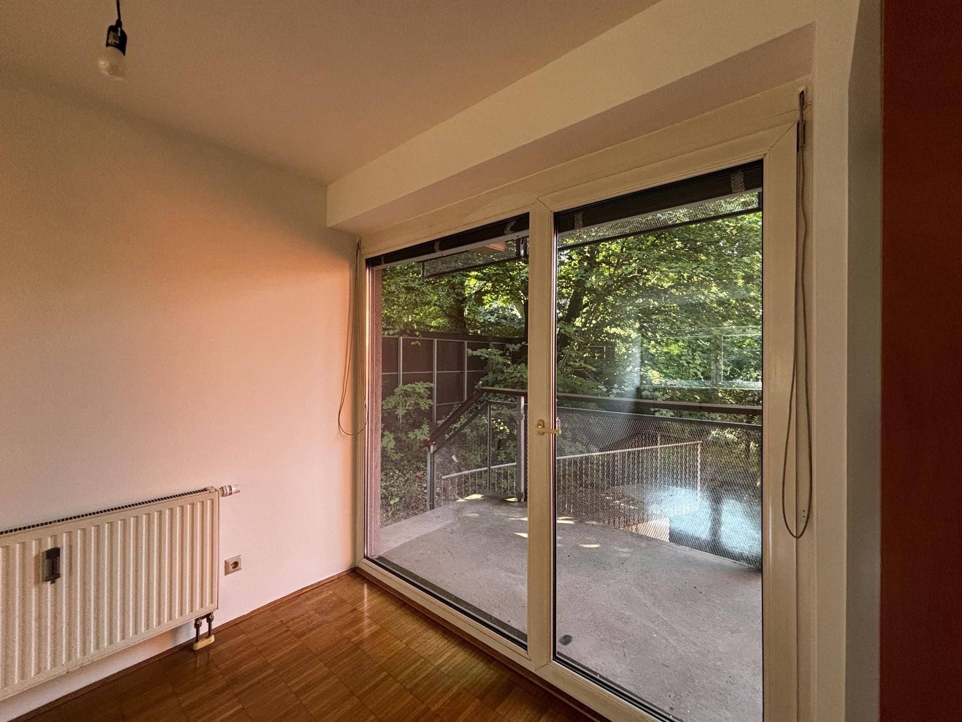 Heller Raum mit Parkettboden und großer Schiebetür, die Zugang zu einem Balkon bietet.