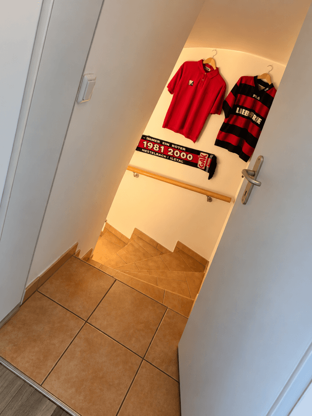 Treppenaufgang mit Fliesenboden und Holzgeländer, dekoriert mit Sporttrikots und Schal.