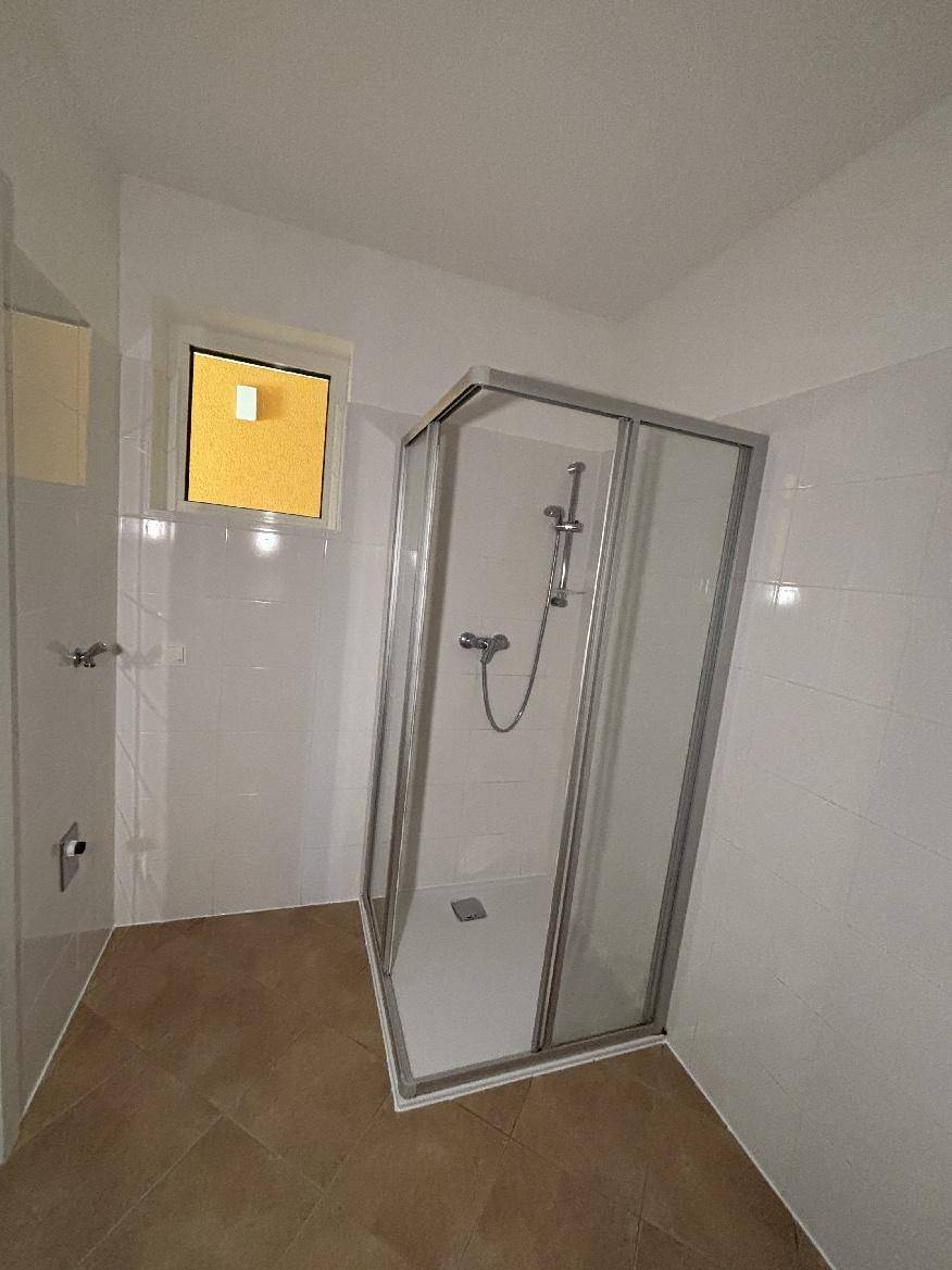 Badezimmer mit Duschkabine, Fenster und weißen Wandfliesen für natürliche Belüftung.