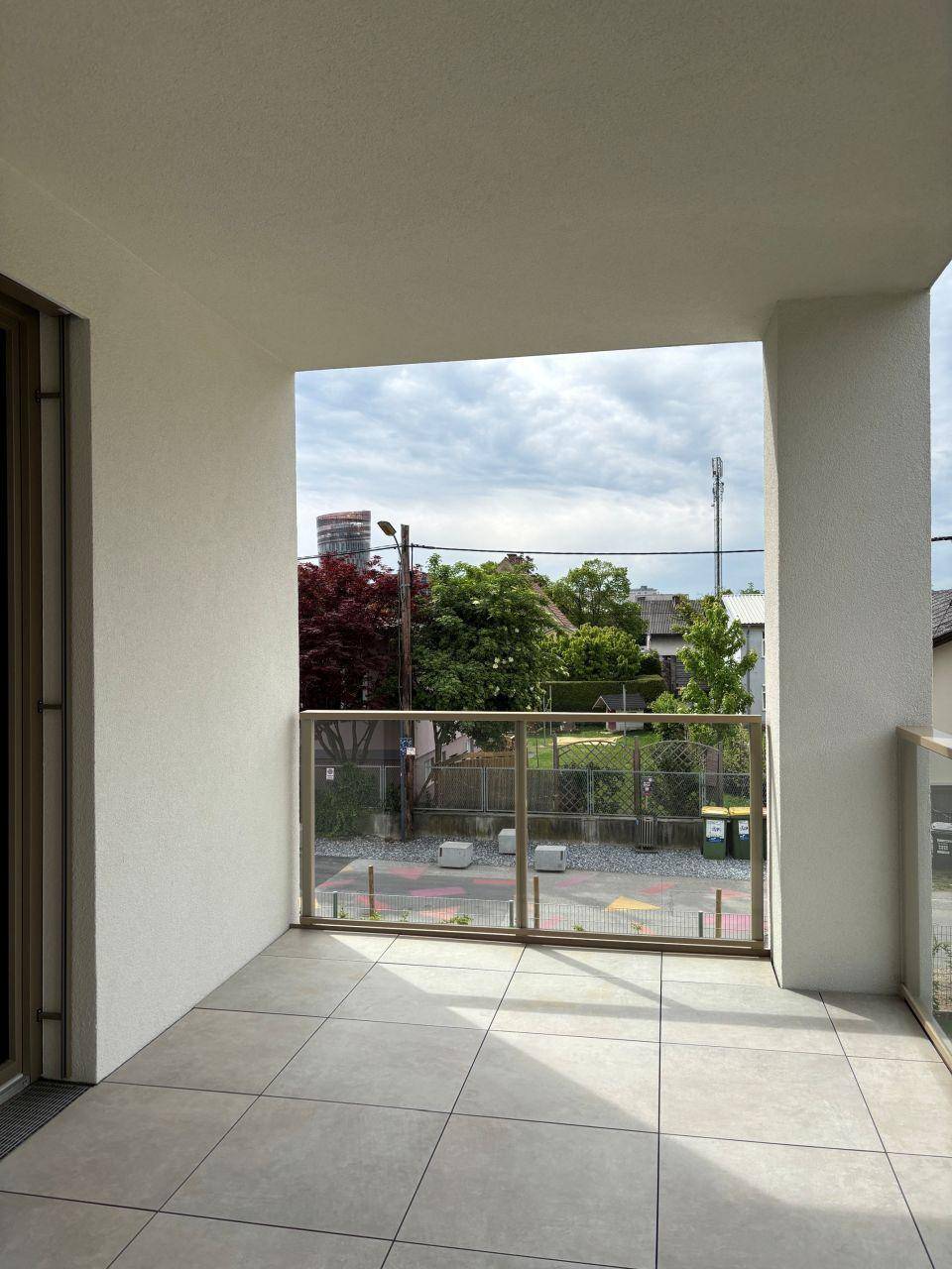 Heller Balkon mit Fliesenboden und Glasgeländer, bietet Blick auf die Umgebung.