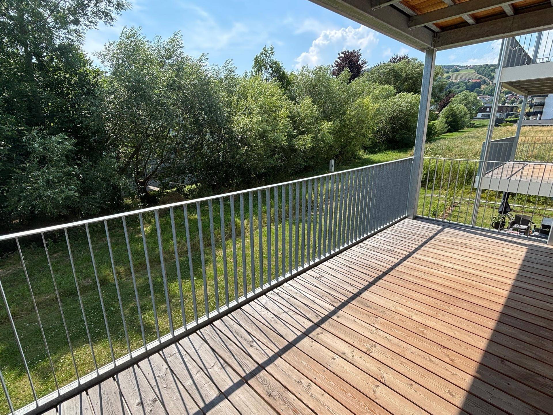 Sonniger Balkon mit Holzbelag und Blick ins Grüne, ideal zum Entspannen im Freien.