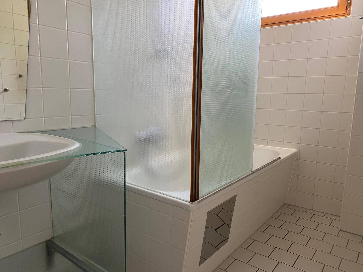 Helles Badezimmer mit weißen Fliesen, Badewanne und Fenster für Tageslicht.
