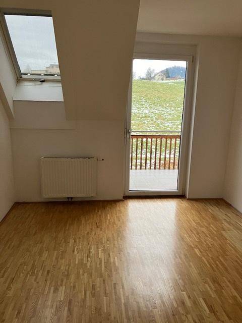 Heller Raum mit Parkettboden, Dachfenster und Zugang zu einem kleinen Balkon.
