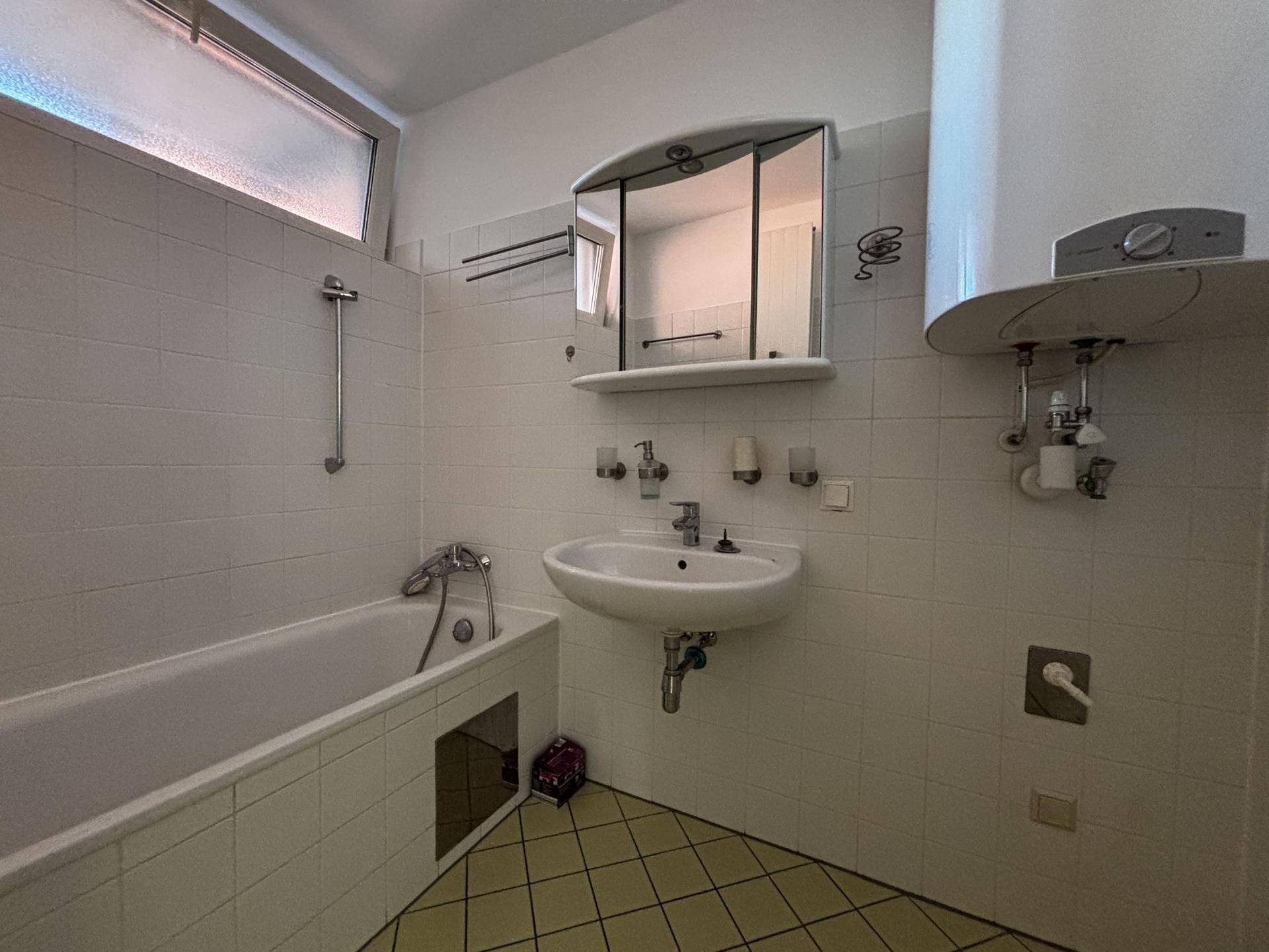 Badezimmer mit Badewanne, Waschbecken, Spiegelschrank und Wandfliesen in hellem Weiß.