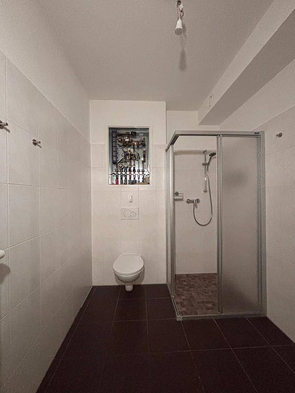 Funktionales Badezimmer mit Duschkabine, WC und dunklen Bodenfliesen.