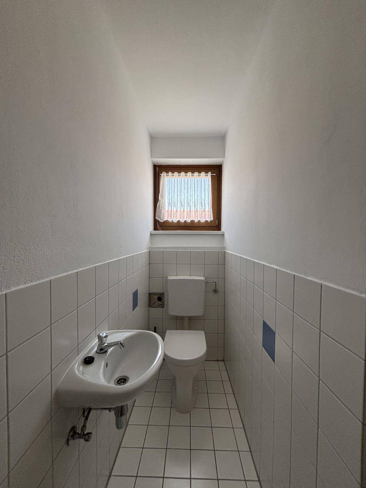 Kleines Gäste-WC mit Fenster, weiß gefliesten Wänden und einem Waschbecken.