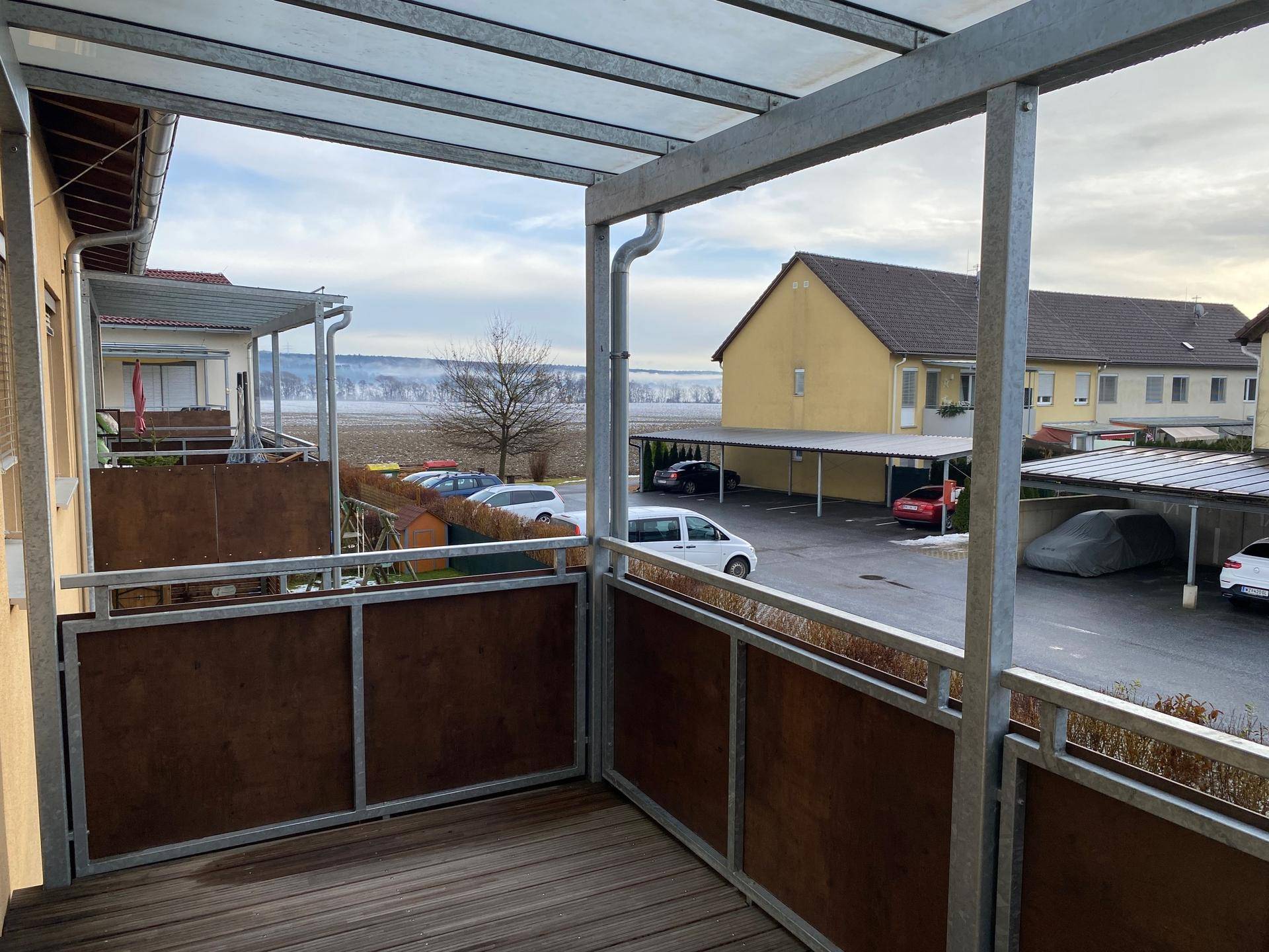 Balkon mit Holzboden, Metallgeländer und Blick auf die Umgebung und Parkplätze.