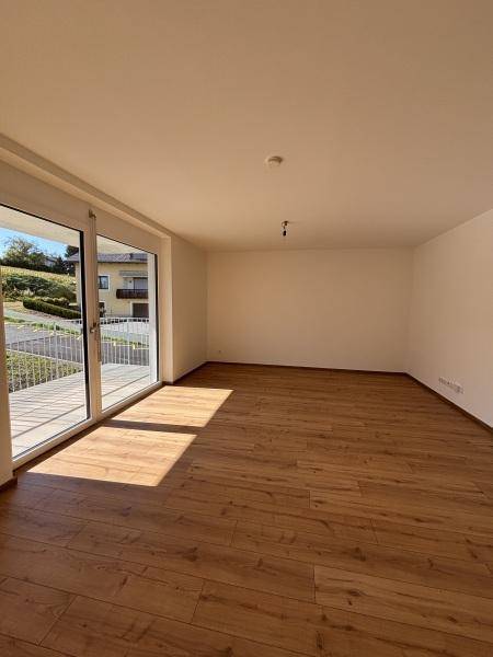 Geräumiges Wohnzimmer mit Holzplankenboden und großer Schiebetür zum Balkon, sehr hell.