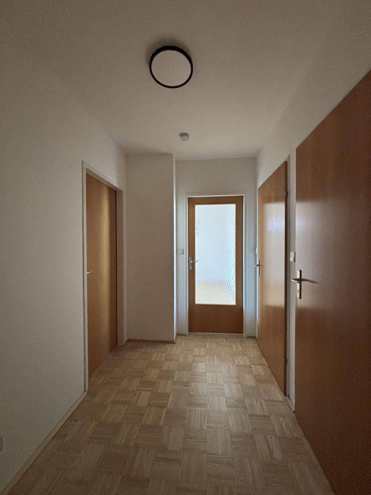 Heller Flur mit Parkettboden und mehreren Holztüren, der verschiedene Räume verbindet.