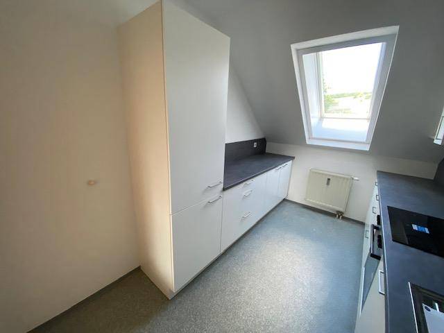 Helle Küche mit Dachfenster, weißen Schränken und dunkler Arbeitsplatte, ideal für Dachgeschosswohnungen.