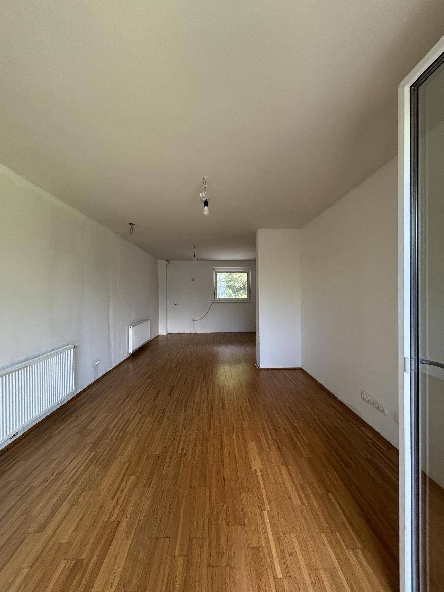 Geräumiges Wohnzimmer mit Holzparkett, großen Fenstern und Zugang zu einem Außenbereich.