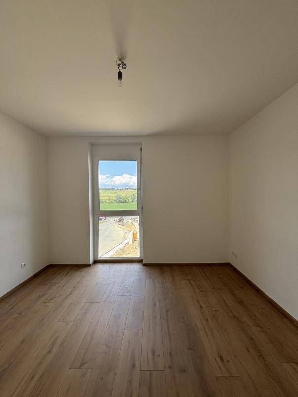 Helles Schlafzimmer mit neuem Holzboden und Blick ins Grüne, bereit zum Einrichten.