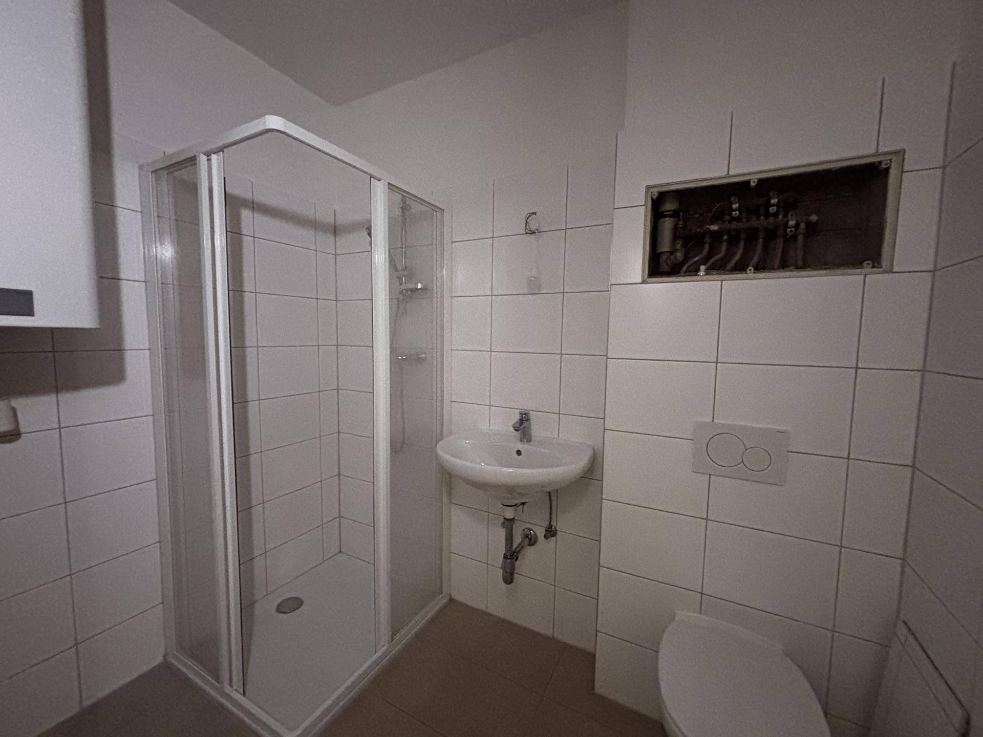 Funktionales Badezimmer mit Duschkabine, Waschbecken und WC, komplett gefliest in Weiß.