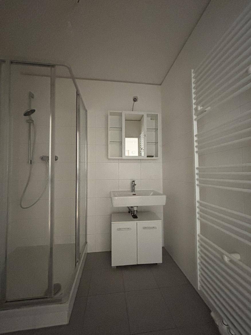 Helles Badezimmer mit Duschkabine, Waschbecken, Spiegelschrank und Handtuchheizkörper.