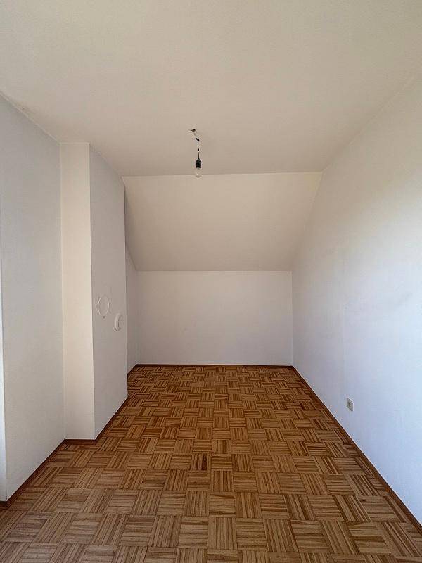 Leeres Zimmer im Dachgeschoss mit Parkettboden und schrägen Wänden, bereit zur individuellen Gestaltung.