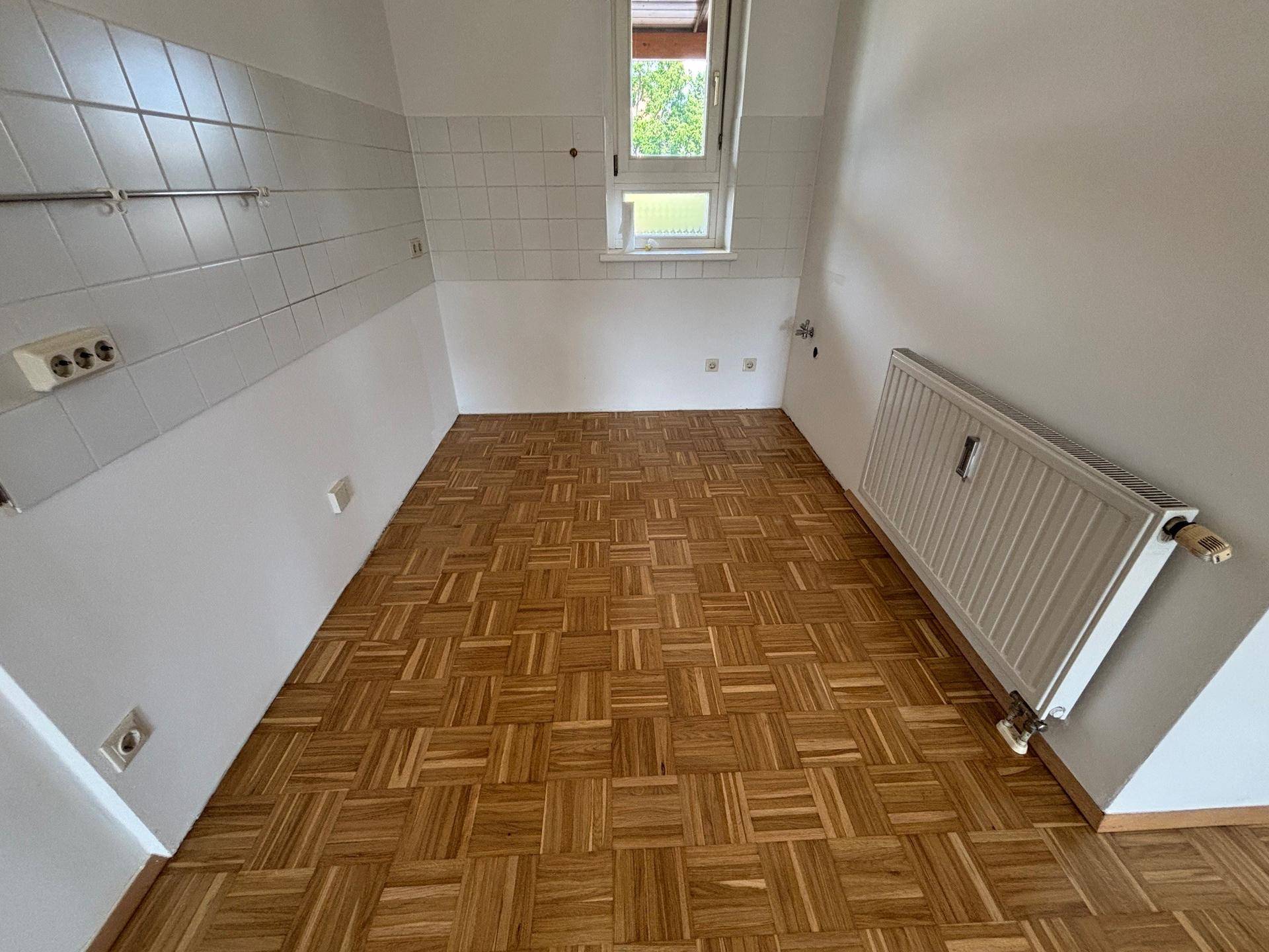 Leerer Küchenraum mit Parkettboden, gefliesten Wänden und Fenster, bereit für die Installation einer Küche.