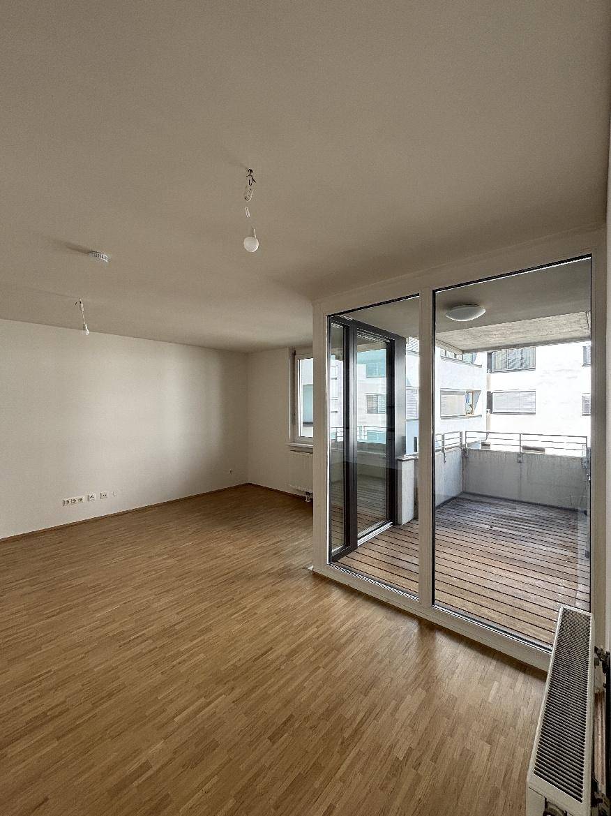 Heller Wohnbereich mit Holzparkettboden und direktem Zugang zu einem sonnigen Balkon.