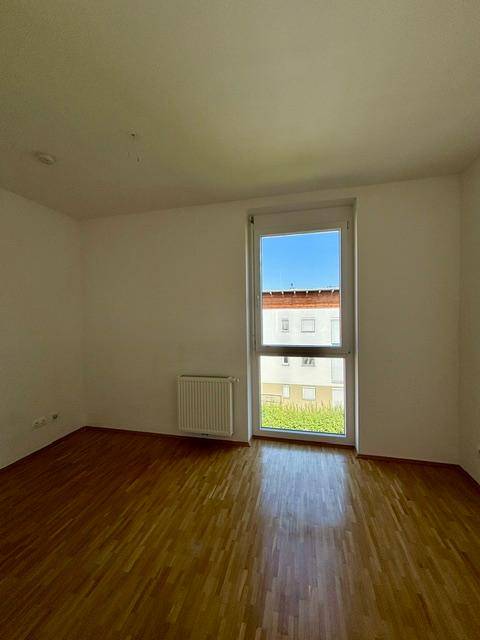Helles Zimmer mit Parkettboden und weiß gestrichenen Wänden, bietet einen Ausblick ins Grüne.