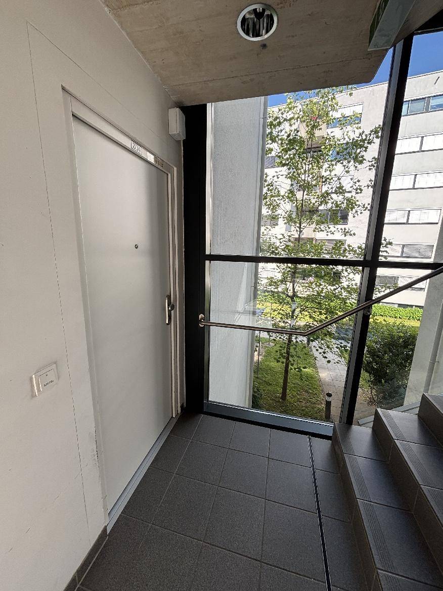 Heller Flur im Gebäude mit Zugang zur Wohnung, großen Fenstern und Treppenhaus.