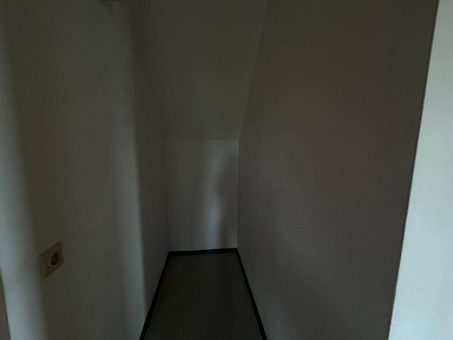 Dunkler, schmaler Abstellraum mit schrägen Wänden und Steckdose.