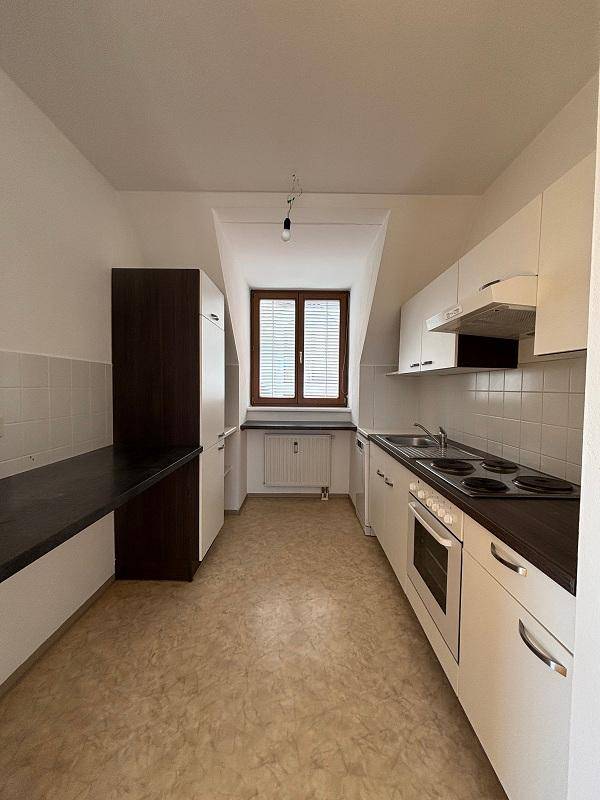 Funktionale Küche mit weißen Schränken, dunklen Arbeitsplatten und einem Fenster unter der Dachschräge.