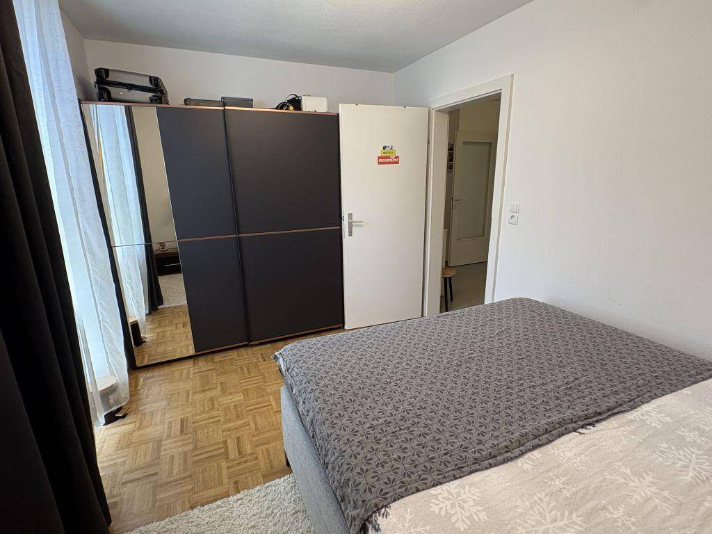 Schlafzimmer mit dunklem Kleiderschrank, Spiegeltüren und Parkettboden, neben einem offenen Durchgang.