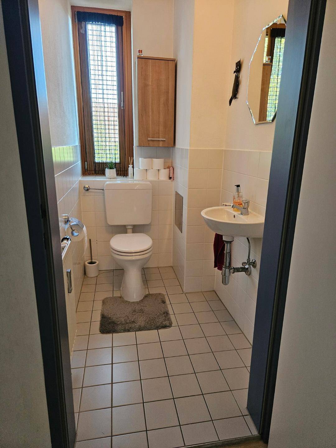 Kleines WC mit Toilette, Waschbecken und Fenster, hell gefliest.