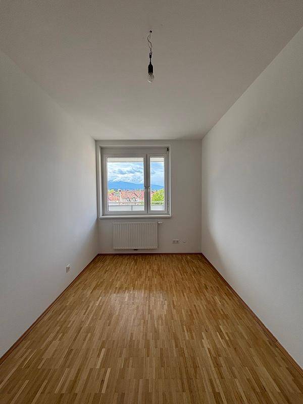 Helles Schlafzimmer mit Parkettboden und Ausblick auf die Umgebung und Berge.